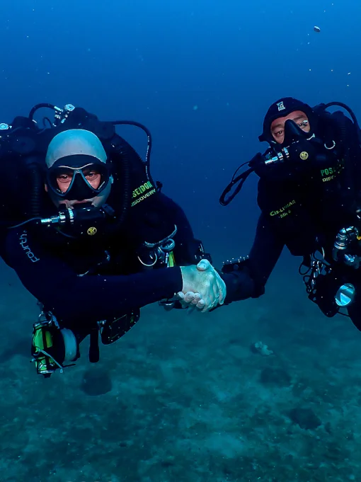 two rebreather divers shaking hands underwater
